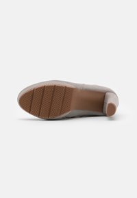 Zapato de ante gris para mujer tumbado de lado, mostrando suela de goma texturada en tono marrón claro y pequeño tacón cuadrado.