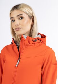 Lys orange softshell-jacka med grå foder, med en hög krage, justerbar huva och framdragkedja. Diskreta sömnadsdetaljer synliga.