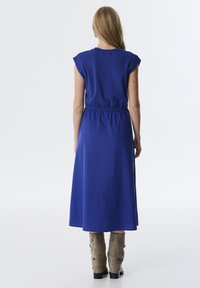 Blaudes Baumwollkleid mit kurzen Ärmeln, elastischem Bund und einem fließenden Design, kombiniert mit beigen Stiefeln bis zur Mitte der Wade mit Knopfdetails.