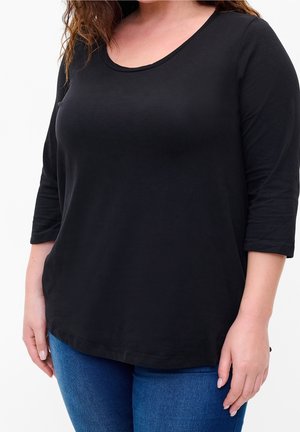 Haut noir léger à manches longues avec un col arrondi et une coupe décontractée, associé à un jean en denim bleu. Texture lisse sur toute la surface.