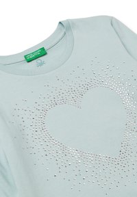 Světle modré bavlněné tričko s designem srdce poskládaného z rozptýlených stříbrných kamínků. Kulatý výstřih a krátké rukávy.
