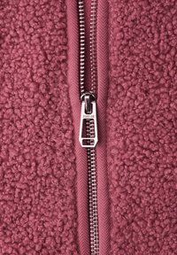 Primer plano de una tela de forro polar texturizada rosa con una cremallera metálica plateada etiquetada "STREET ONE" que corre verticalmente por el centro.