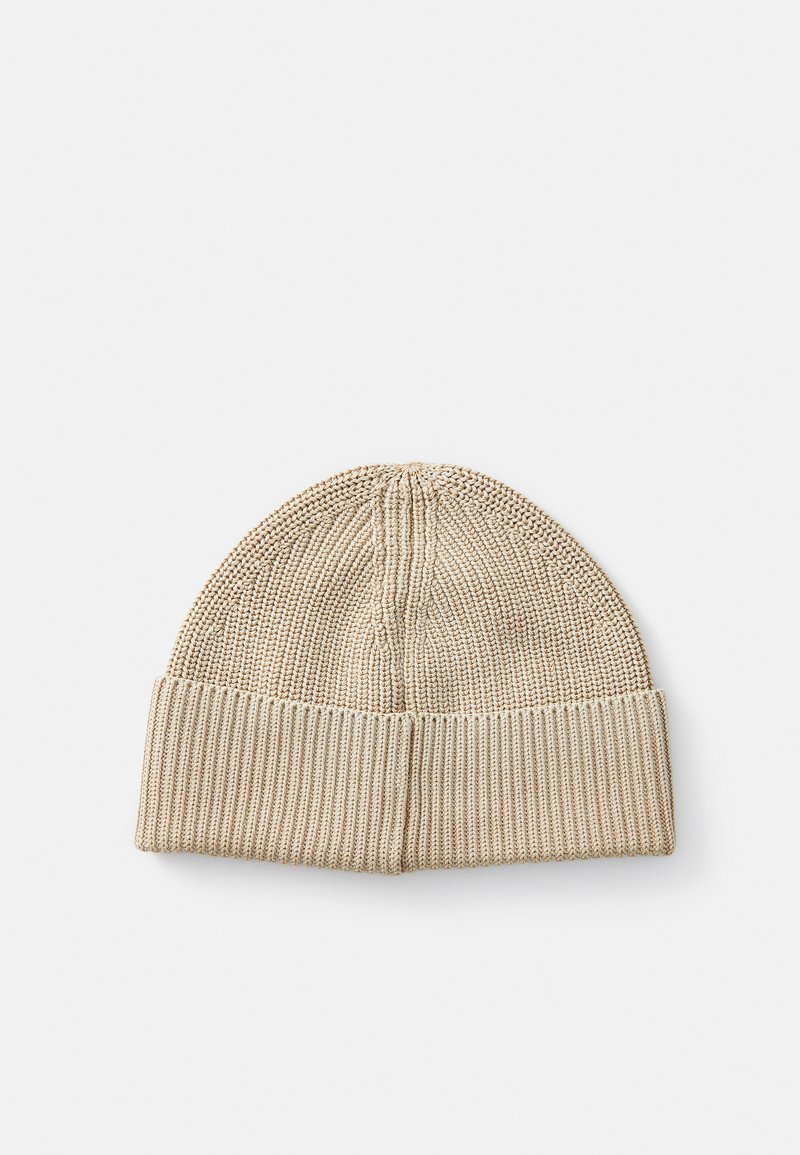 Berretto di maglia beige con risvolto a coste. Il materiale è morbido e testurizzato, presenta una parte superiore arrotondata e cuciture uniformi.