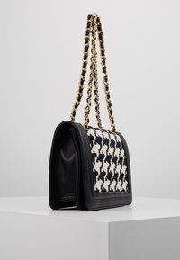 Black leather handbag with a white and black houndstooth pattern. Features a gold chain strap and a structured shape with a flap closure.