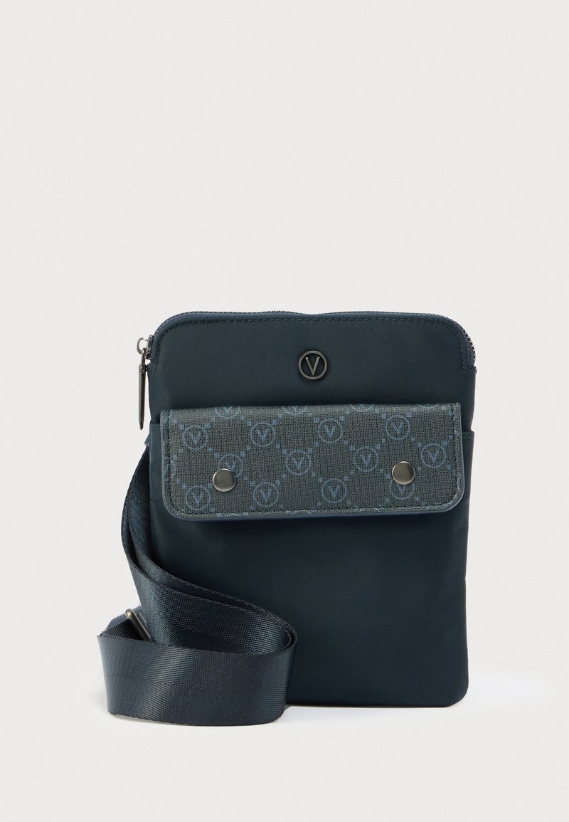 Mala tamnoplava torbica na preklop s podesivim remenom, prednji džep s preklopom i kopčama na drukere te zatvarač na vrhu.