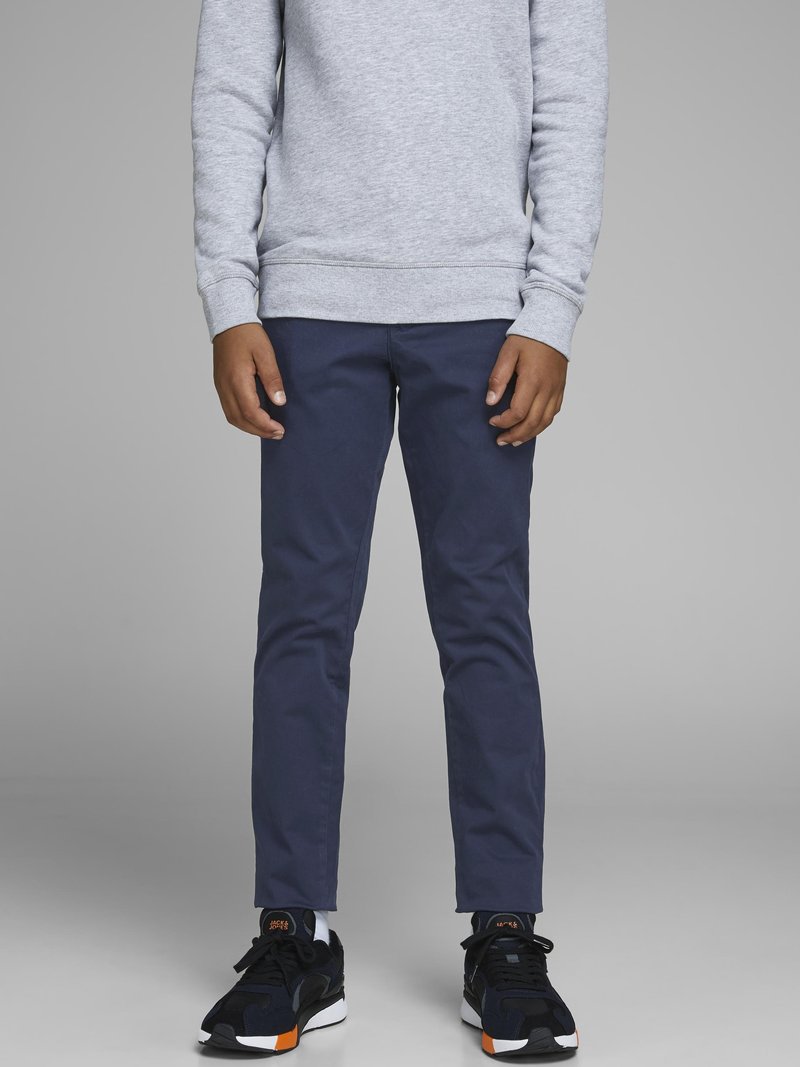 Pantalones ajustados azul marino de mezcla de algodón, combinados con zapatillas negras con acentos naranjas y suelas blancas, y una sudadera gris en la parte superior.