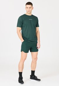 Grünes sportliches Shirt und Shorts aus atmungsaktivem Material, mit dezenten Logodetails, kombiniert mit schwarzen Laufschuhen und Socken.