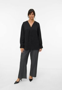Black long-sleeve blouse with a V-neck, button front closure, and puffed shoulders, paired with gray wide-leg trousers and black pointed heels.