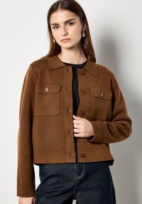 Bruine wollen jack in een mix met een kraag, twee borstzakken, knoopsluiting en ribbeltextuur. Gecombineerd met donkere denim broek.