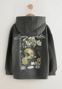 Haut de sweatshirt gris foncé avec un grand motif de crâne entouré de fleurs. Comprend un texte blanc et des coordonnées en bas.