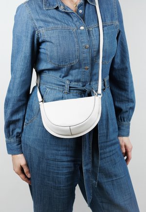 White leather crossbody bag with a rounded top, thin strap, and subtle stitching details, worn over a denim jumpsuit.