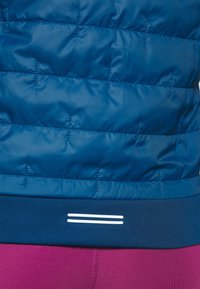 Veste matelassée bleue avec une texture lisse, dotée d'une ceinture bleu foncé et de deux bandes blanches horizontales en bas.