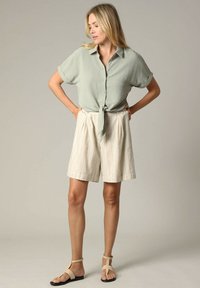 Lichtgroene korte mouwen button-up shirt met geknoopte voorkant, gecombineerd met hooggeknipte crèmekleurige shorts met verticale strepen en platte sandalen.