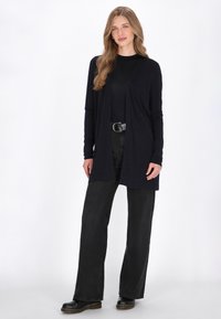 Navyblauer Cardigan mit offenem Front aus weichem Stoff, kombiniert mit schwarzen weiten Jeans und schwarzen Stiefeln. Lange Ärmel und lässige Passform.