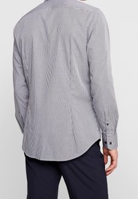 Košile s dlouhým rukávem v kostkovaném vzoru, převážně černobílá. Má knoflíkové manžety a zakřivený lem, vyrobena z lehkého materiálu.