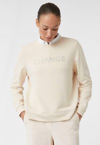 Felpa beige con la scritta "CHANGE" realizzata in borchie in rilievo. Presenta un scollatura rotonda e maniche lunghe, realizzata in morbido tessuto misto cotone.