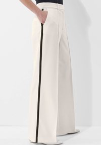 Lange broek in roomkleur met een rechte silhoutte, voorzien van een contrasterende zwarte zijstreep en zijzakken. Soepele stoftextuur.
