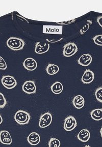 T-shirt bleu marine avec des motifs de visages souriants couleur crème. Présente un col rond et un tissu doux et texturé. Étiquette de marque : Molo.