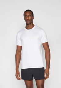 Λευκό πουκάμισο με κοντά μανίκια από απαλό ύφασμα, με στρογγυλή λαιμόκοψη και άνετη εφαρμογή, σε συνδυασμό με μαύρο σορτς.