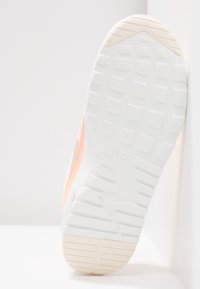 Vita och persikofärgade Nike-sneakersula med fyrkantigt och randigt mönster, där Nike-logotypen syns i mitten.