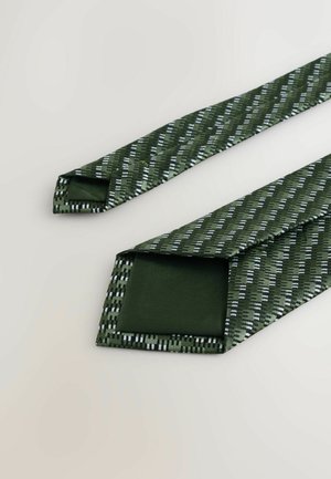 Žalia kaklaraištis su tekstūruotu raštu, kuriame yra geometrinės linijos baltomis ir sidabro akcentais. Pagamintas iš lygaus audinio, su smailiu galu ir plačia pelekine dalimi.