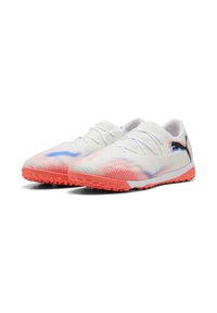 Zapatos de fútbol blancos con una parte superior texturizada, que presenta un diseño degradado en rosa y azul, suela de goma naranja y acento de logo negro.