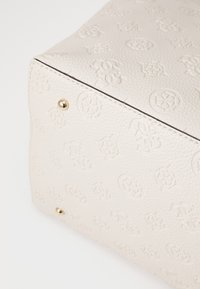 Sac en cuir blanc arborant des motifs floraux et de logo en relief, avec des clous dorés à la base pour plus de détails et de stabilité.