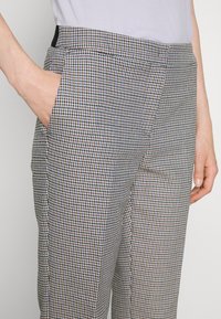 Houndstooth-mönstrade byxor i ljusblått, brunt och svart. Har en slät yta, sidofickor och en skräddarsydd passform.