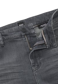 Mörkgrå denimbyxor med dragkedja och knappstängning. Har en märkesetikett vid midjan och en diskret vävd struktur.