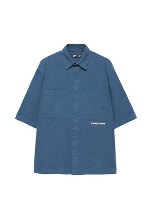 Chemise bleue à manches courtes, boutonnée, avec deux poches poitrine et texte blanc "STWDSTUDIO" sur la poche inférieure droite.