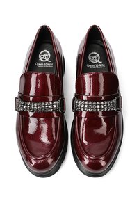 Mocassini in pelle verniciata bordeaux con punta arrotondata, dotati di una fascia decorativa nera con borchie e una suola in gomma nera bassa.