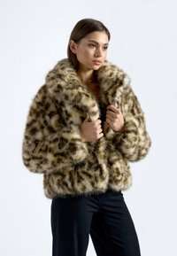 Lažna krznena jakna sa točkicama u nijansama smeđe i krem. Ima širok ovratnik i kutijasti kroj. Mekana tekstura.