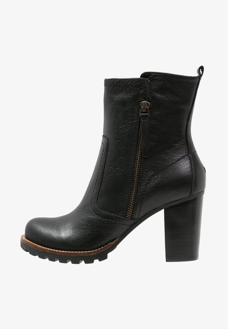 Bottine noire en cuir avec fermeture éclaire latérale, bout rond, talon épais, et surface texturée pour une meilleure adhérence. Possède une bordure marron contrastante.