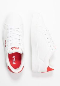 Vita sneakers med texturerad ovandel, snörning och röda detaljer på hälen och innersulan. Textlogotyp på tungan.