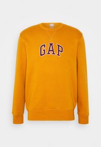 Sudadera de cuello redondo amarilla con "GAP" bordado en púrpura oscuro en el pecho. Puños y dobladillo de canalé, tejido suave.