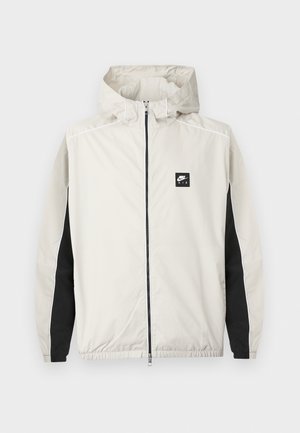 Ανοιχτό γκρι αθλητικό μπουφάν Nike Air με φερμουάρ, κουκούλα και μαύρες πινελιές κατά μήκος του εσωτερικού μέρους των μανικιών.