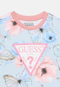 Φωτεινό μπλε μπλουζάκι με ροζ floral και πεταλούδα σχέδιο, με ένα ροζ γκλίτερ τρίγωνο λογότυπο στο κέντρο και ροζ λαιμόκοψη.