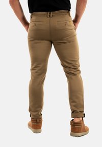 Pantalons khaki ajustés, fabriqués à partir d'un tissu léger. Dotés de deux poches arrière avec fermetures à bouton et d'accents de couture visibles.