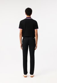Zwarte polo met contrasterende kraag en mouwafwerkingen in blauw, rood en wit, gecombineerd met zwarte broek en beige schoenen.