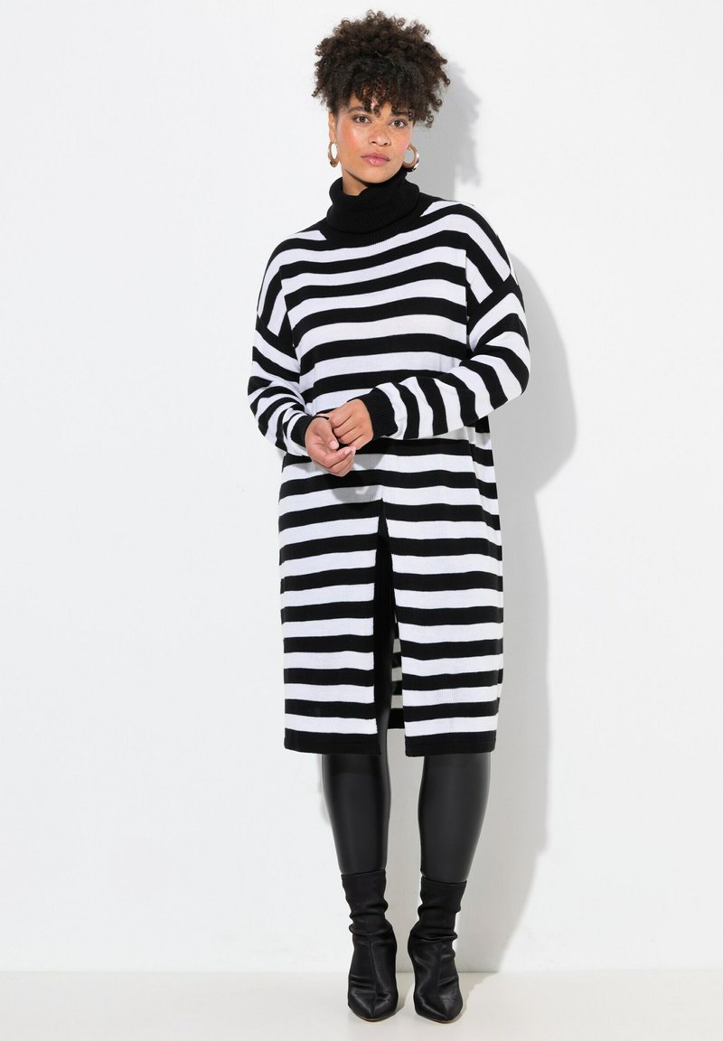 Abito a maglia a righe bianche e nere con colletto alto, maniche lunghe, spacco laterale, abbinato a leggings neri aderenti e stivaletti.