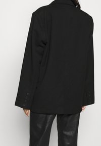 Musta bleiseri, jossa on istuva muotoilu, notched-kaulus ja kuusi nappikoristetta hihoissa. Sujuva rakenne, minimalistinen tyyli.