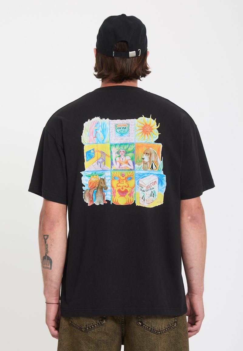 Άνδρας που φοράει μαύρο καπέλο και μαύρο T-shirt με πολύχρωμο γραφικό εννέα πλαισίων που απεικονίζει ήλιο, σκύλο, καρέκλα και προσώπα στην πλάτη.