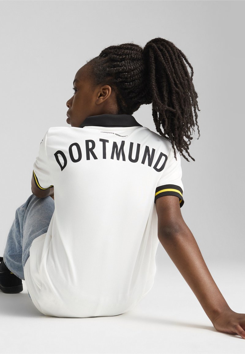 Balta polo marškinėliai su juodu koloritu ir geltonais akcentais, su užrašu "DORTMUND", išryškintu ant nugaros, su tekstūruotu audiniu.