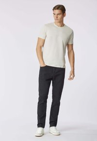T-shirt in cotone beige chiaro con collo rotondo e maniche corte, abbinata a jeans neri attillati e sneakers bianche.