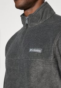 Γκρίζος φλις πούλντερ με σχέδιο quarter-zip, διαθέτει λογότυπο Columbia στο στήθος και υφή στην επιφάνεια.