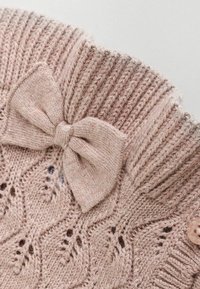 Section d'un pull en tricot rose clair avec un col côtelé, un motif en dentelle complexe et un grand nœud décoratif au niveau du col.