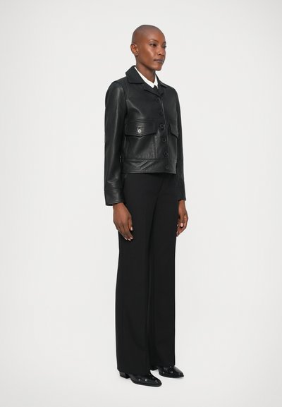 Zwarte leren jas met cropped ontwerp, knoopsluiting, twee voorkbakken, gecombineerd met zwarte hoge taillebroeken en zwarte schoenen.