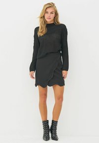 Black knit sweater with a textured pattern, paired with a black skirt featuring a curved hem. Footwear includes black studded ankle boots.