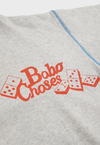 Sivi pamučni materijal s velikim crvenim grafikonom koji prikazuje natpis "Bobo Choses" s ilustriranim dominama ispod teksta. Naglašen plavim šavovima.