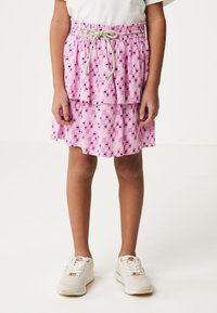 Gonna a strati rosa con motivi geometrici in viola e verde. Vita elastica con lacci verdi. Indossata con sneakers bianche.